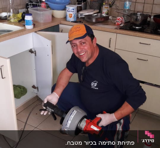 אינסטלטור מחזיק כלי עבודה ליד ארון מטבח פתוח